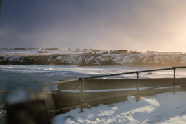 Coastal picture of the Isle of Lewis, with stormy sky, snow, and wild seas beside a pier